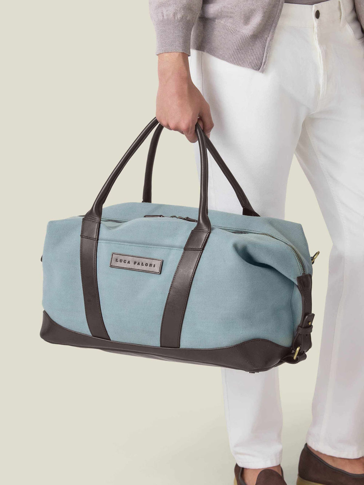 A man holding the Luca Faloni Canvas Bag in French Blue, detailed with dark brown leather handles and trim.