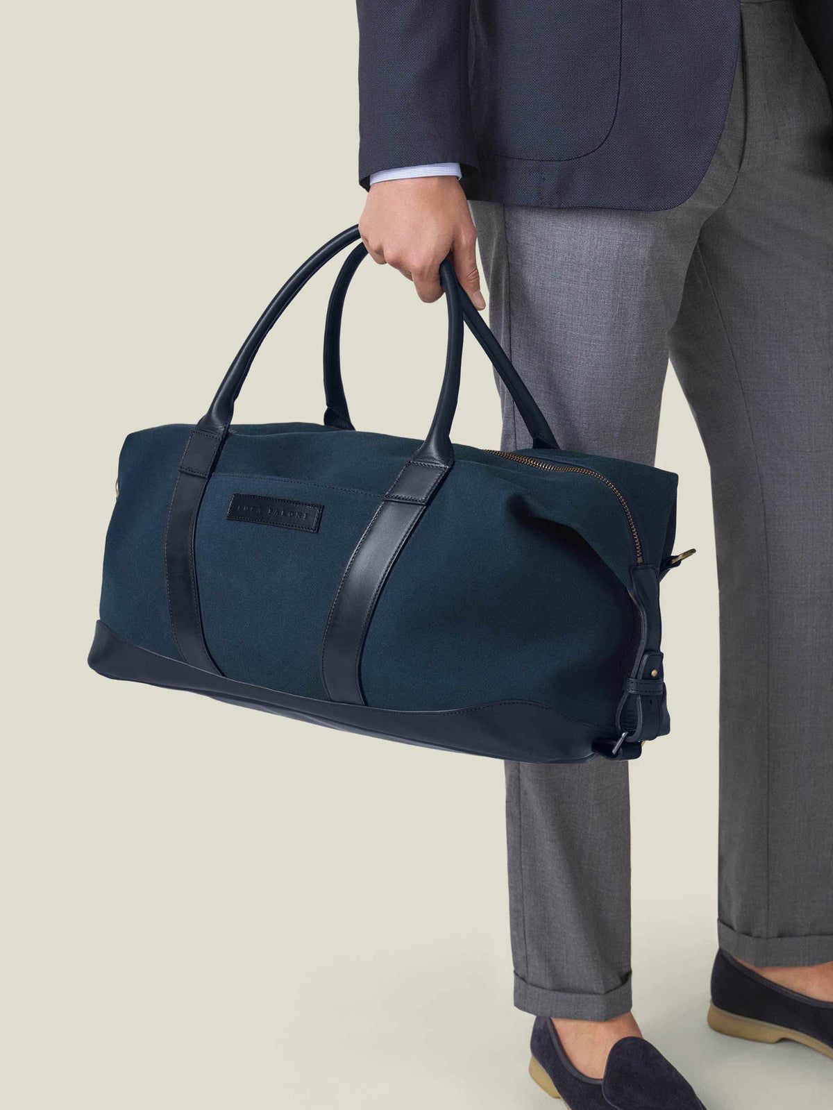 A man holding the Midnight Blue Canvas Weekender bag, styled with a navy blazer and grey trousers.