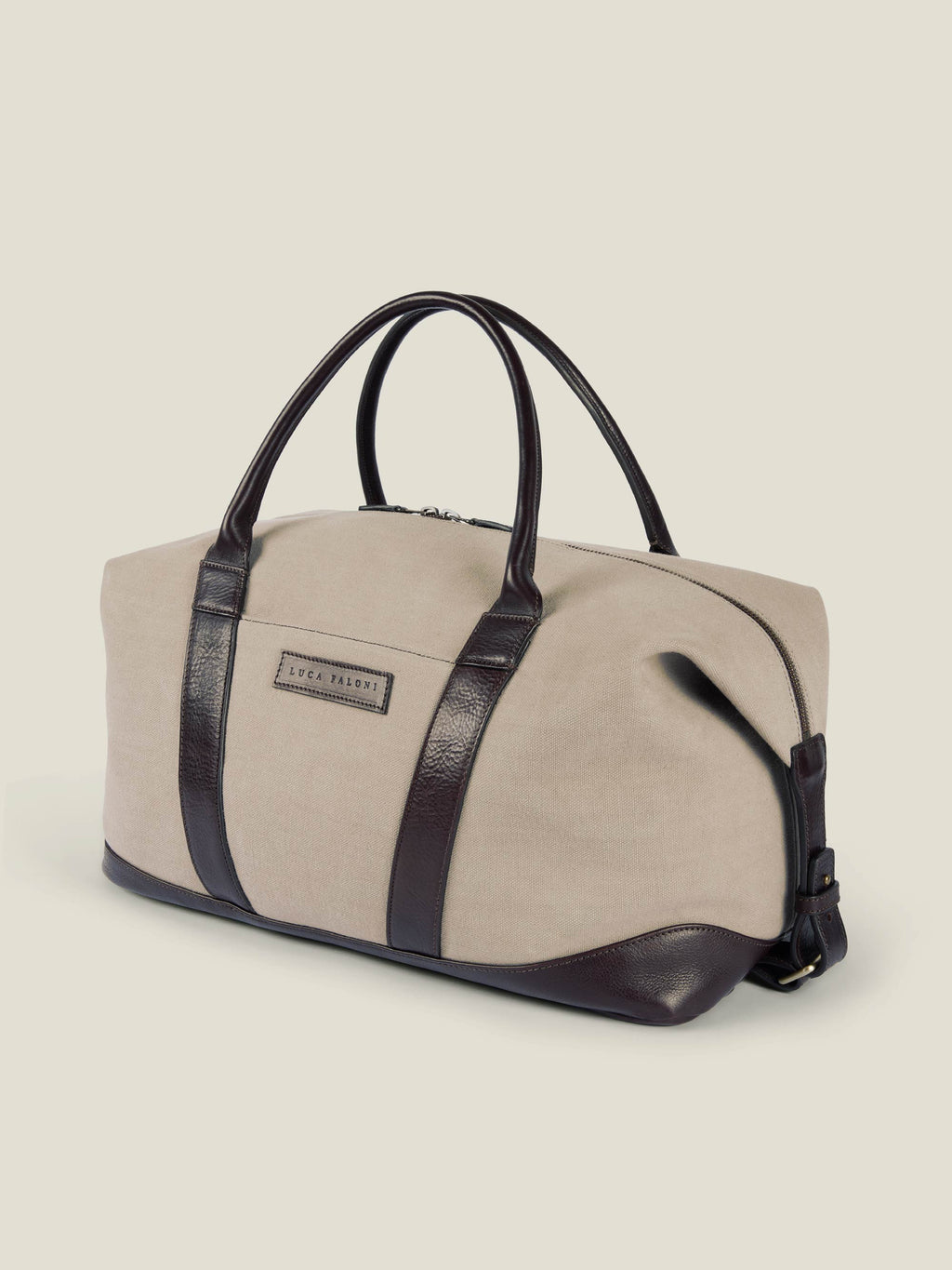 Side view of the Luca Faloni Canvas Weekender Bag in sand, featuring dark brown leather handles, trim, and base.