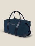 A three-quarter view of the Luca Faloni Canvas Weekender Bag in midnight blue with black leather handles and trim.