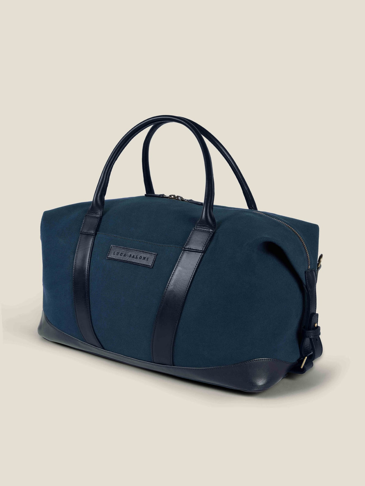 A three-quarter view of the Luca Faloni Canvas Weekender Bag in midnight blue with black leather handles and trim.