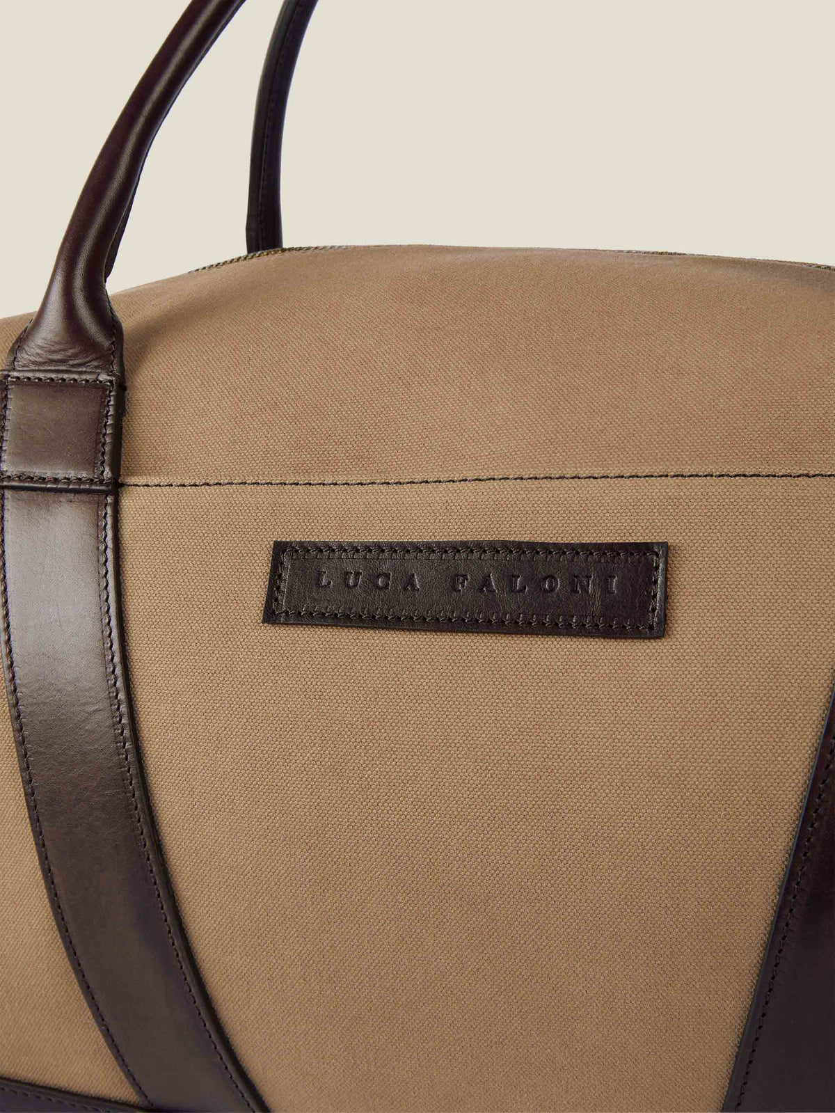 Close-up of the embossed Luca Faloni leather logo on the caramel brown canvas bag, with dark brown leather handle details.