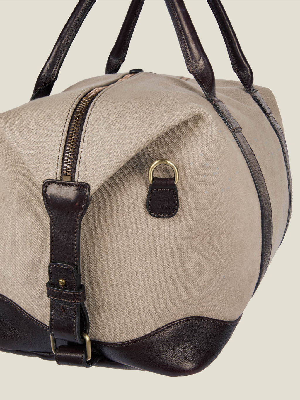 Close-up of the Luca Faloni sand canvas weekender bag, highlighting the dark brown leather trim, handles and brass D-ring.