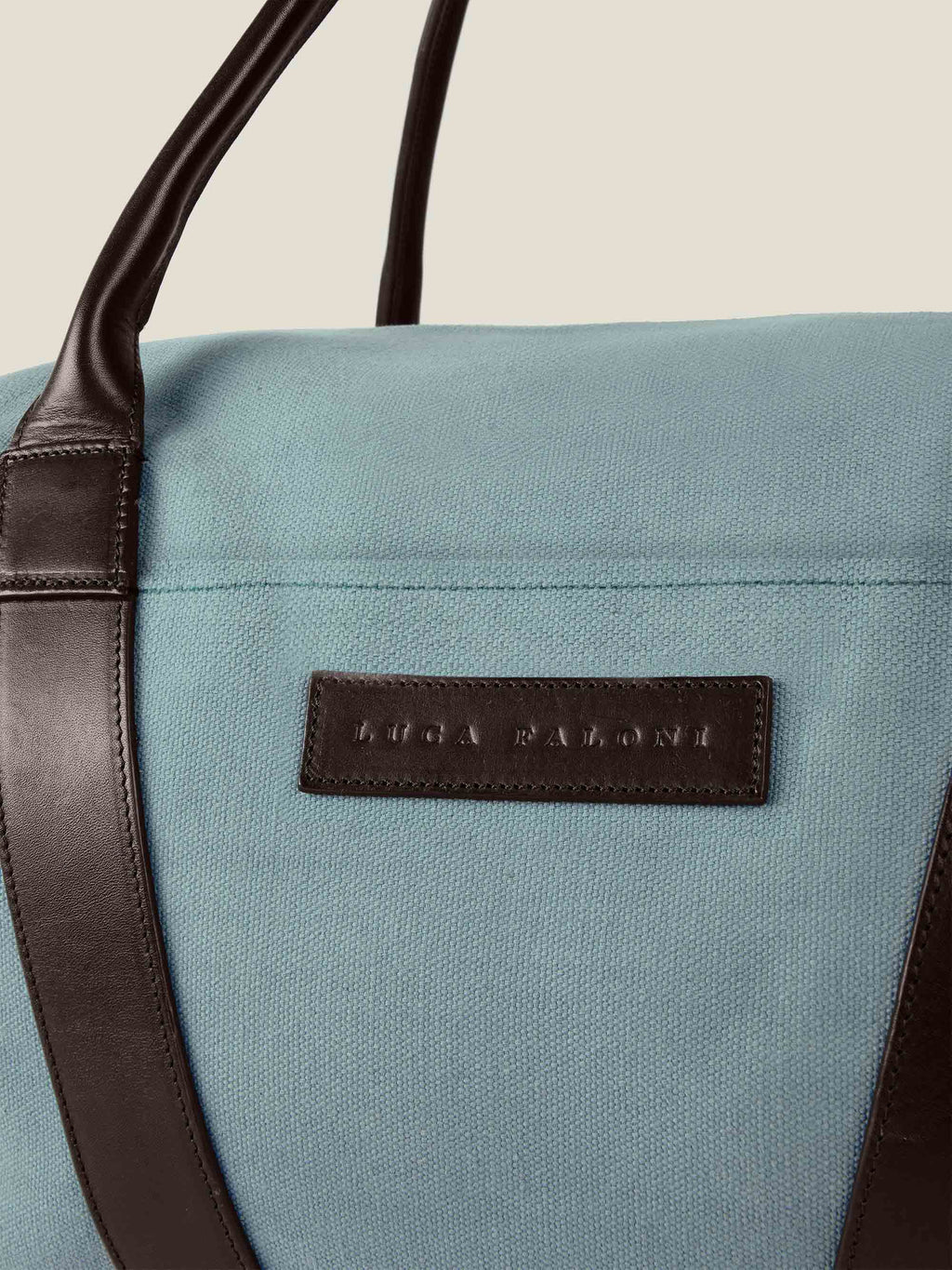 Close-up of the French Blue Canvas Bag, highlighting the embossed Luca Faloni logo on a dark brown leather patch.