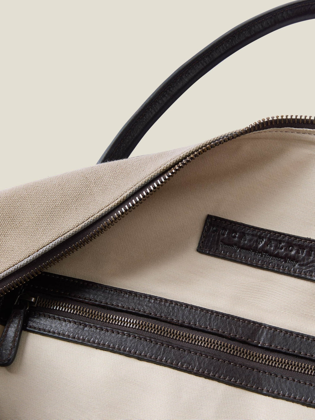 Close-up of the sand Canvas Bag's interior, showing the natural canvas lining, internal zip pocket and embossed leather logo.