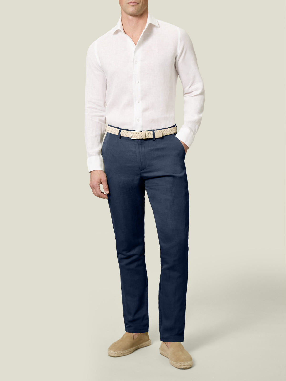 Model wears Luca Faloni's Midnight Blue Linen Cotton Trousers with a white shirt, woven belt, and beige espadrilles.