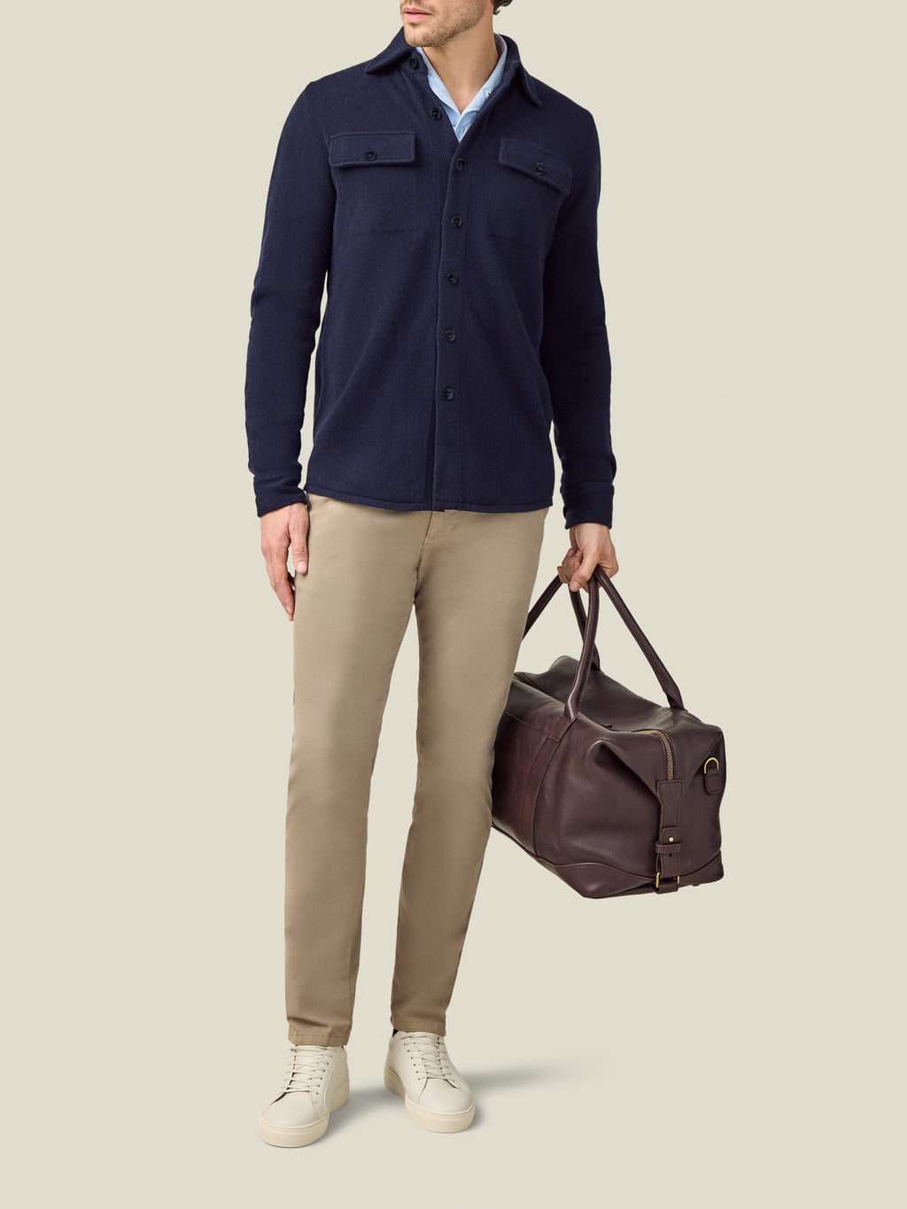 A model wears the Luca Faloni Cashmere Overshirt in Midnight Blue with beige trousers, white sneakers, and a leather bag.